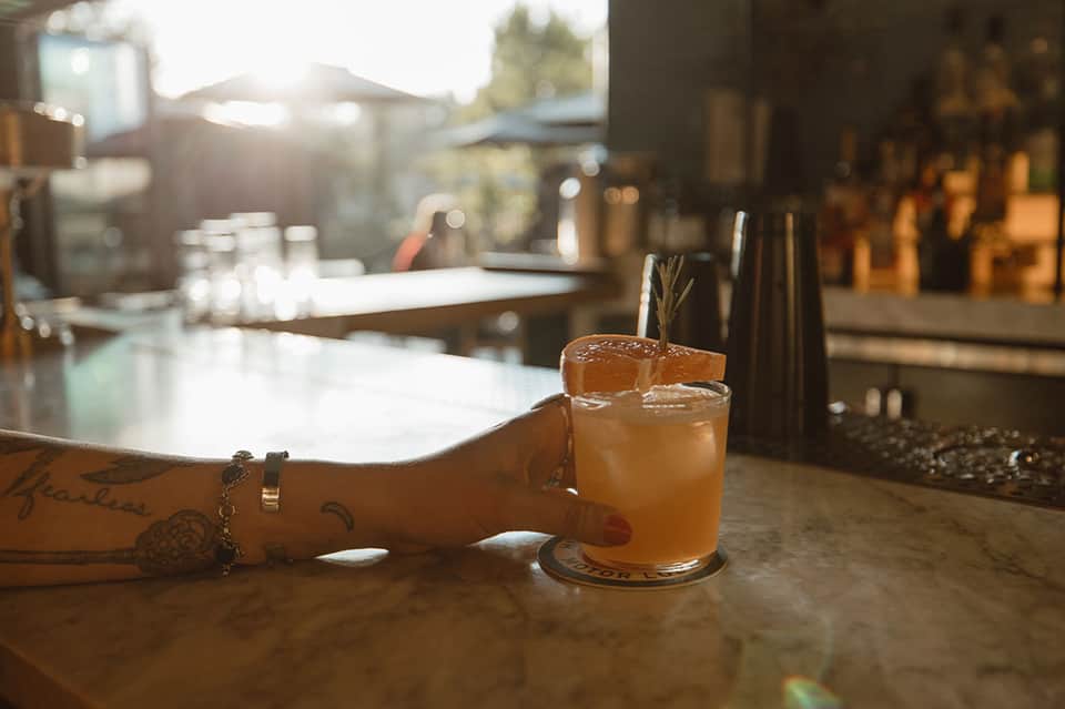 Cocktail with rosemary garnish on bar counter with sunset ambiance