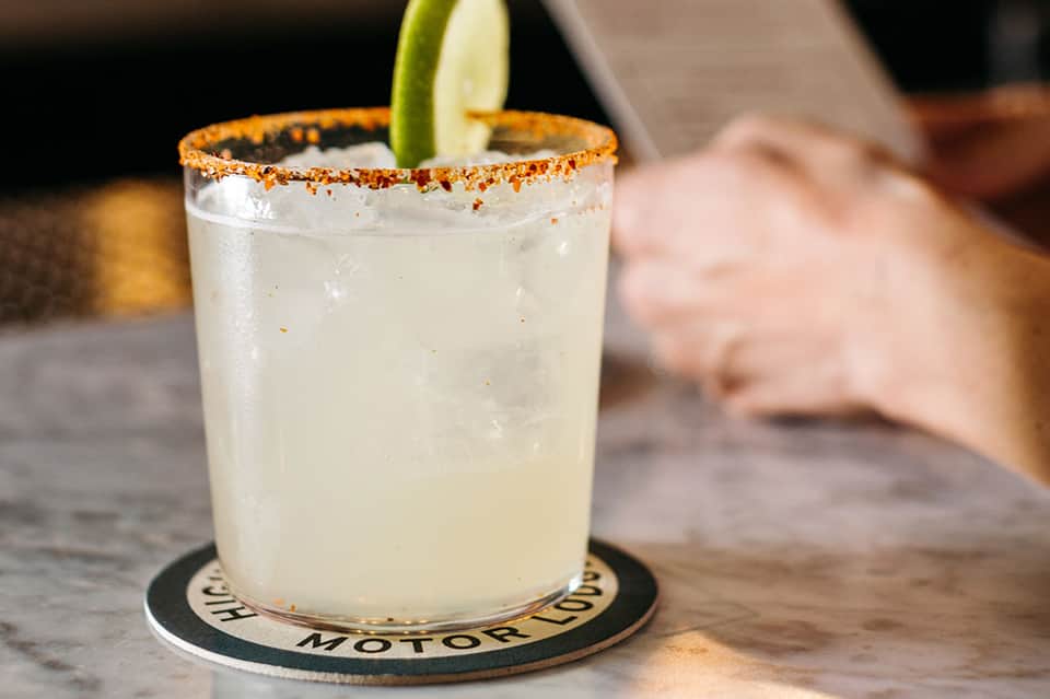 Spicy margarita with salt rim and lime wheel on dark coaster at bar