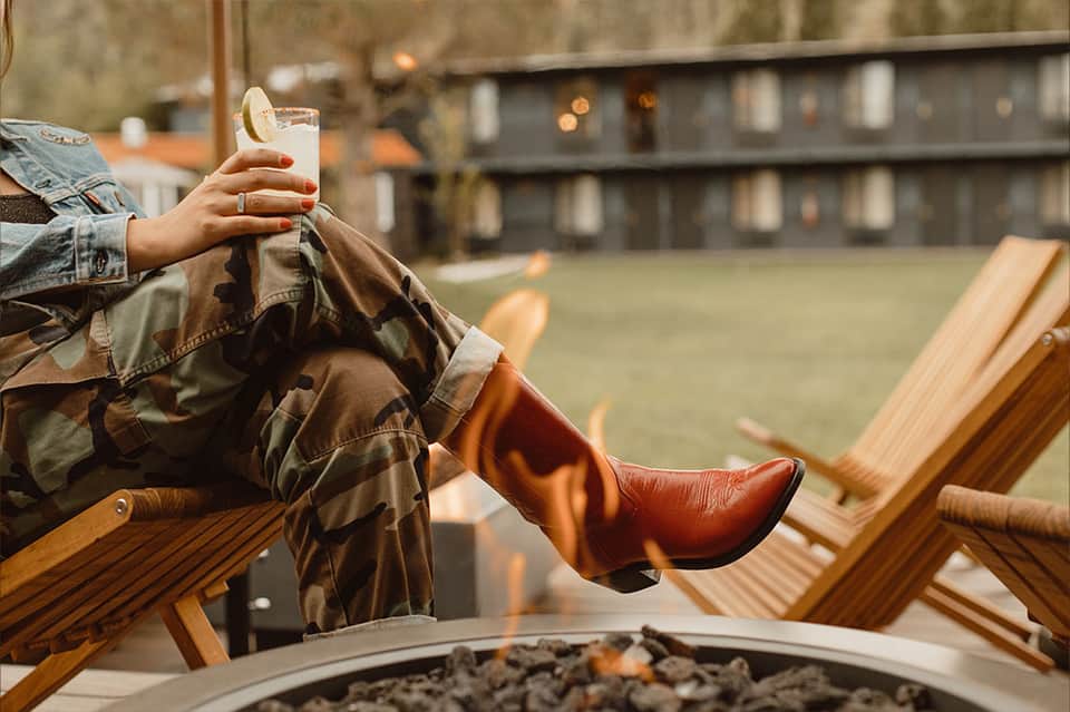 Person relaxing in wooden lounge chair holding a drink overlooking resort grounds
