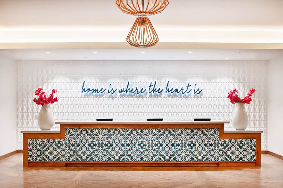 Modern hotel reception desk with blue neon sign reading 'home is where the heart is'