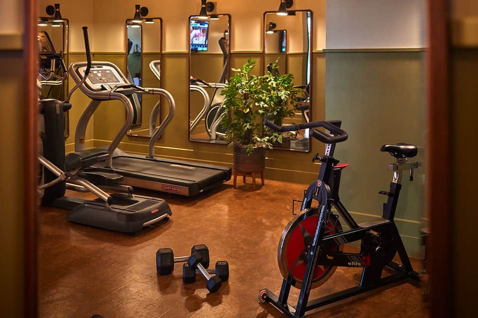 Modern fitness center with cardio equipment, mirrors, and plants in warm-toned interior