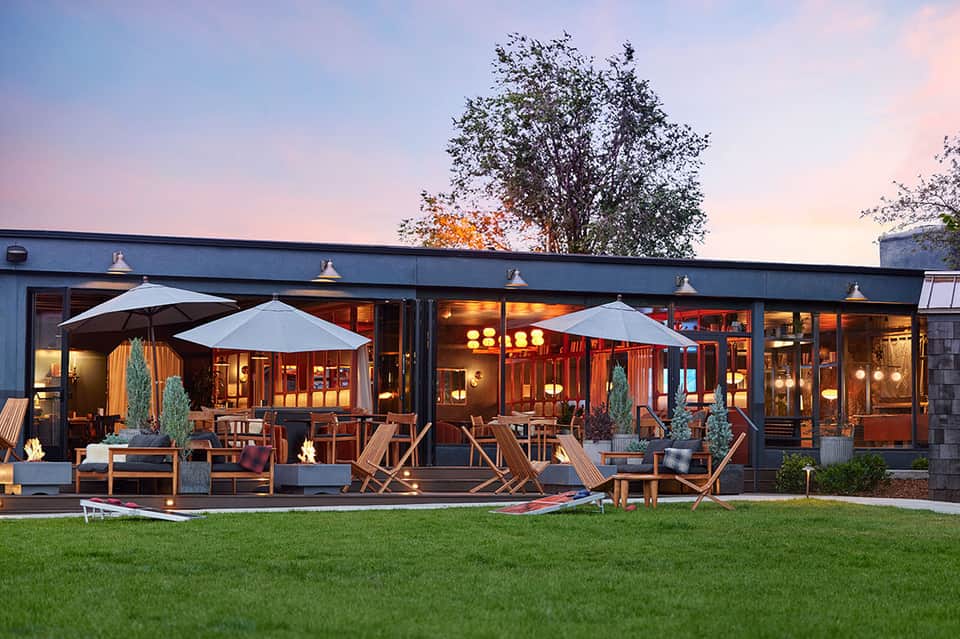 Modern waterfront restaurant pavilion at dusk with umbrellas, wooden furnishings, and illuminated interior
