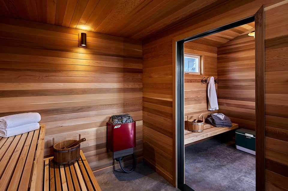 Wooden sauna interior with benches, heater, and frosted glass partition door