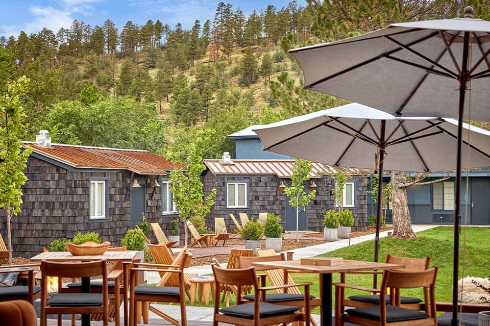 Modern mountain lodge patio with umbrellas, wooden furniture, and forested valley backdrop