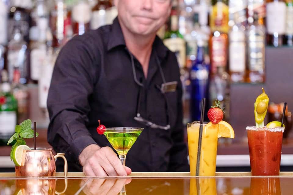 Bartender preparing colorful cocktails at upscale bar with multiple garnishes and spirits