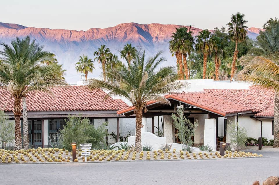 Desert resort building with terracotta roof, palm trees, and mountains in background