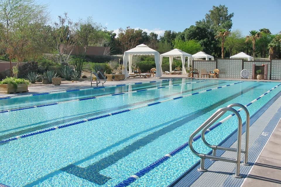 Lap pool with lane dividers and white cabanas in desert landscape with palm trees