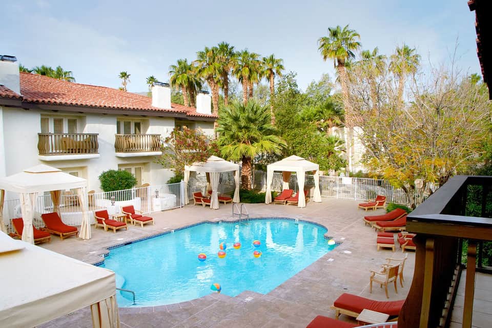 Resort pool with colorful umbrellas, white cabanas, palm trees, and Spanish colonial architecture