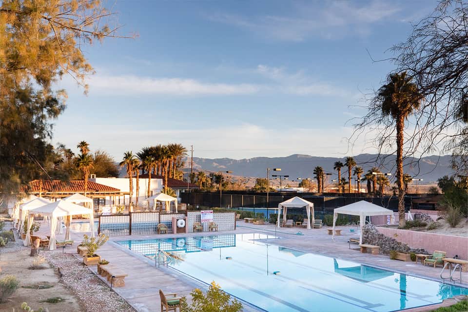 Desert resort pool with white cabanas and mountains in the distance