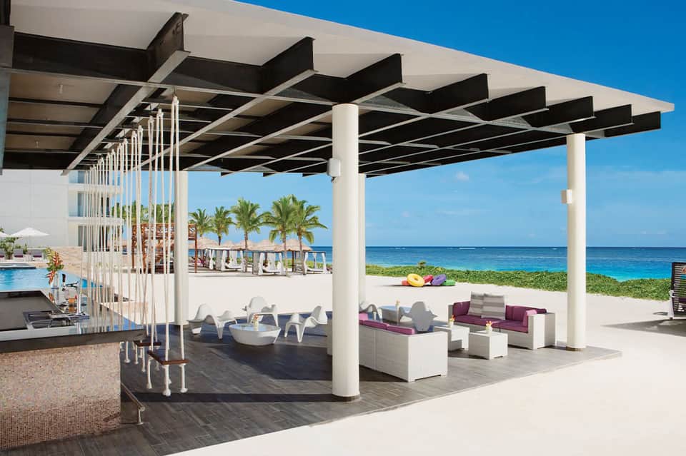 Beachfront resort pergola with black and white geometric shade structure, ocean view, and lounge seating