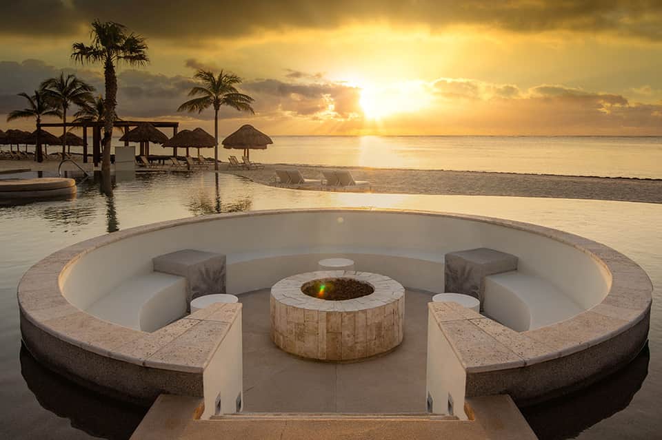 Oceanfront fire pit with curved stone seating overlooking beach at golden sunset with palm trees