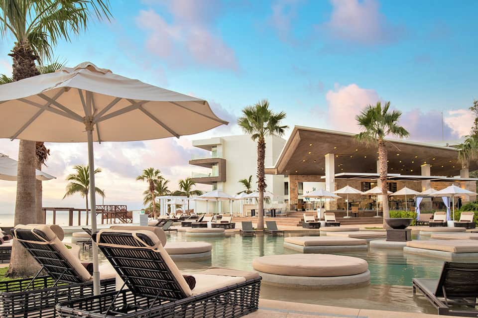 Luxurious resort pool deck with loungers, umbrellas, palm trees, and modern architecture
