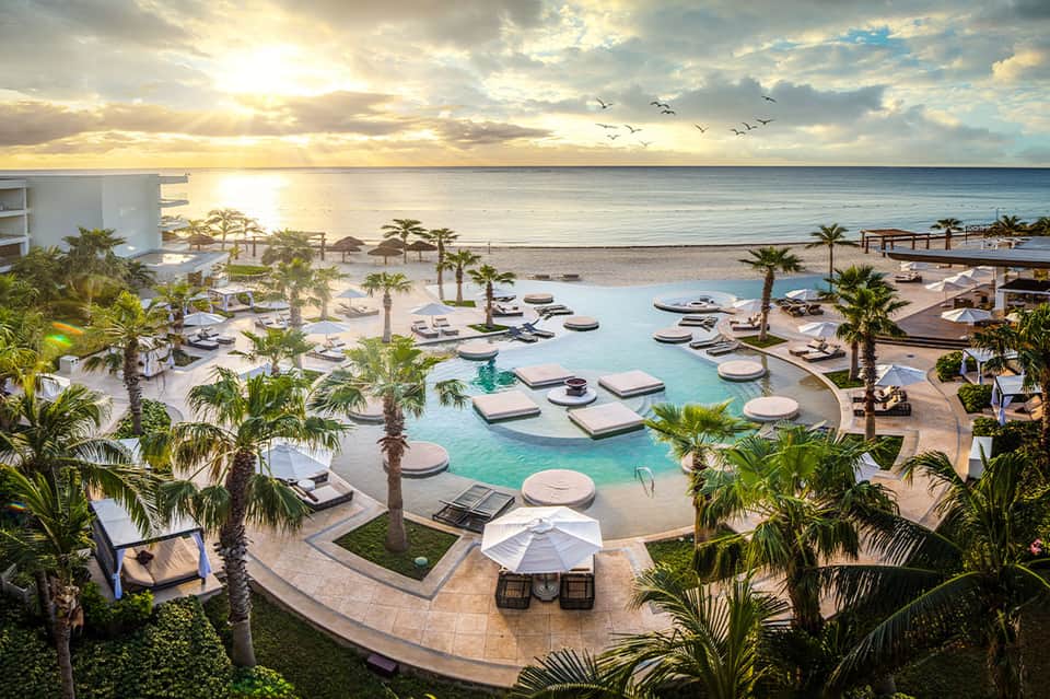 Beachfront resort with infinity pool, palm trees, loungers, and sunset ocean view