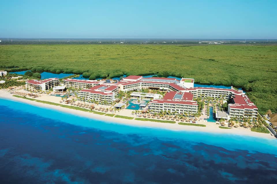 Aerial view of beachfront all-inclusive resort with red roofs, pools, and turquoise ocean