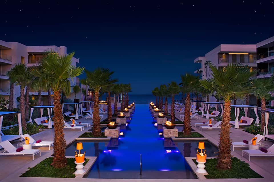 Luxury beachfront resort with infinity pool, palm trees, and ocean view at night
