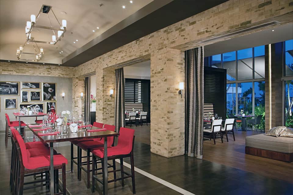 Modern luxury dining room with red chairs, long black table, brick walls, and expansive window views