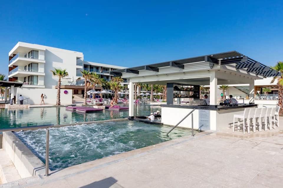 Modern resort pool with white bar structure, palm trees, and beachfront building