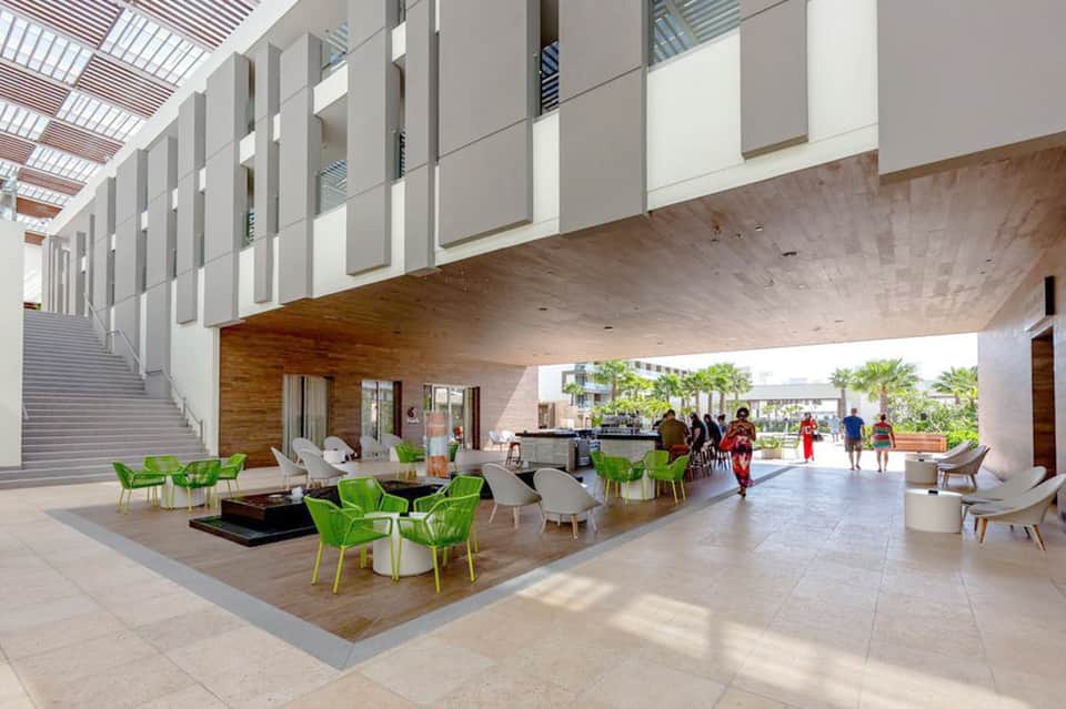 Modern resort lobby with bright natural lighting, green chairs, wooden accents, and open architectural design