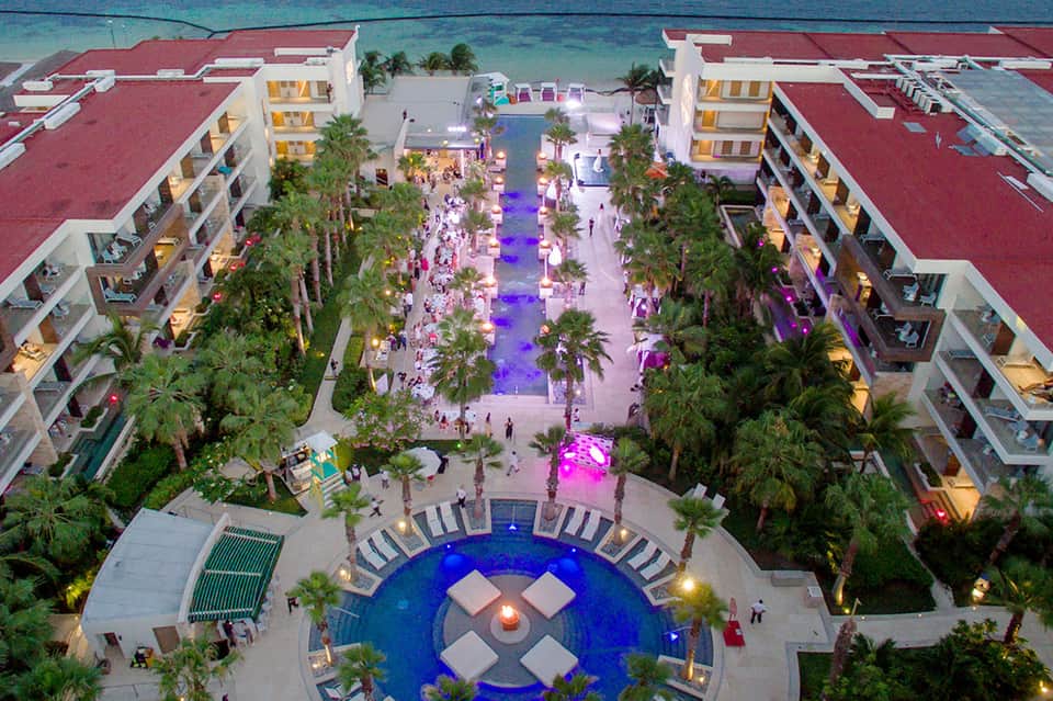 Aerial view of beachfront resort at night with palm-lined promenade, illuminated courtyard, and ocean backdrop