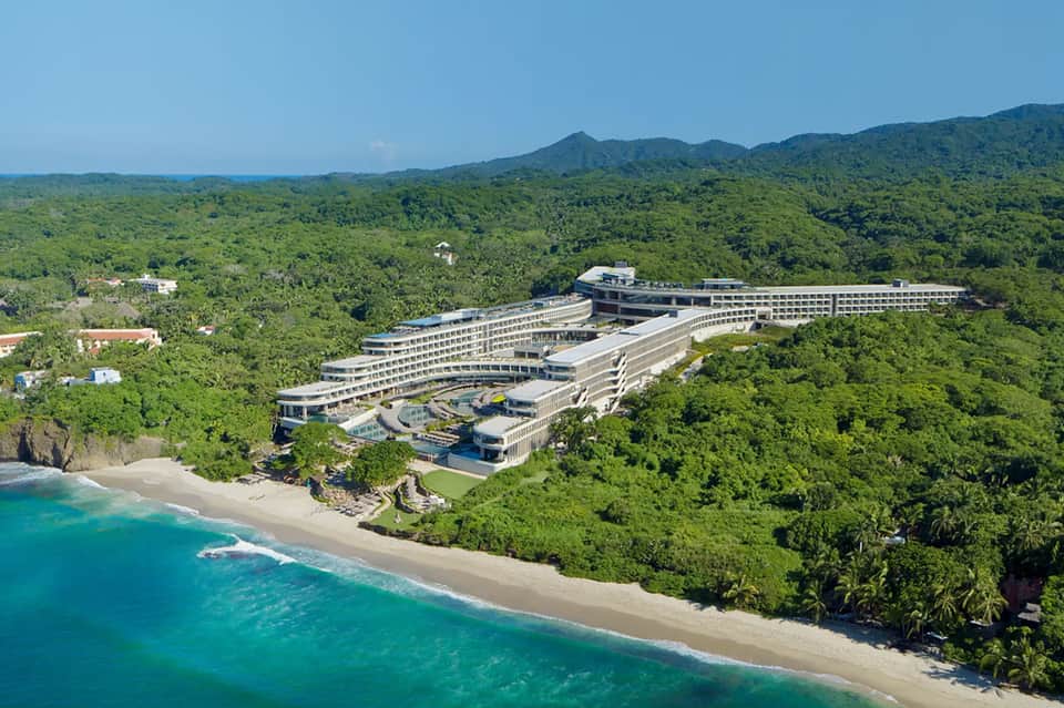 Aerial view of cliffside resort nestled in tropical jungle overlooking turquoise ocean beach