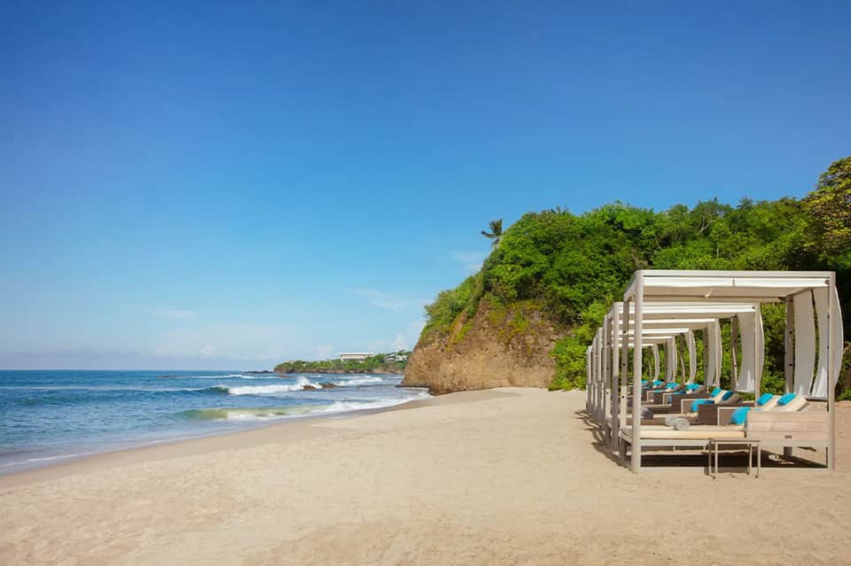Beach cabanas on sandy shore with ocean waves and cliff vegetation