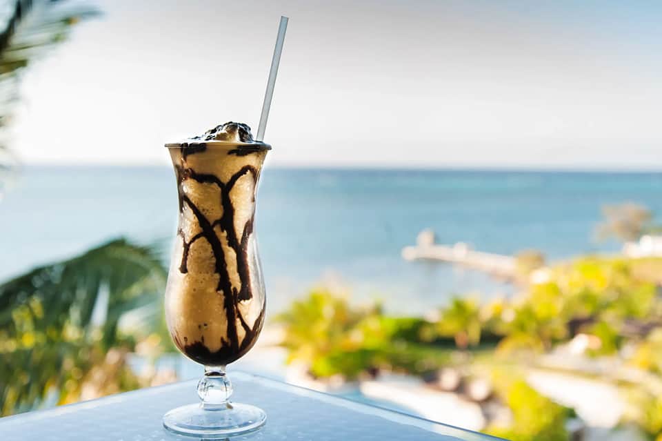 Tropical cocktail with chocolate drizzle on table overlooking ocean and palm trees
