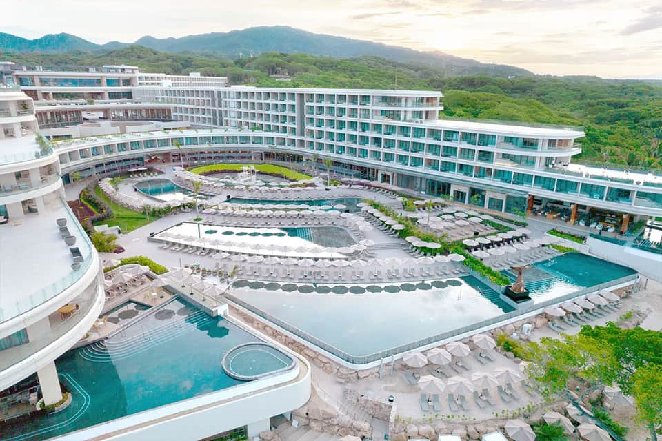 Aerial view of luxury resort with multiple pools, hot springs, and mountainous landscape backdrop