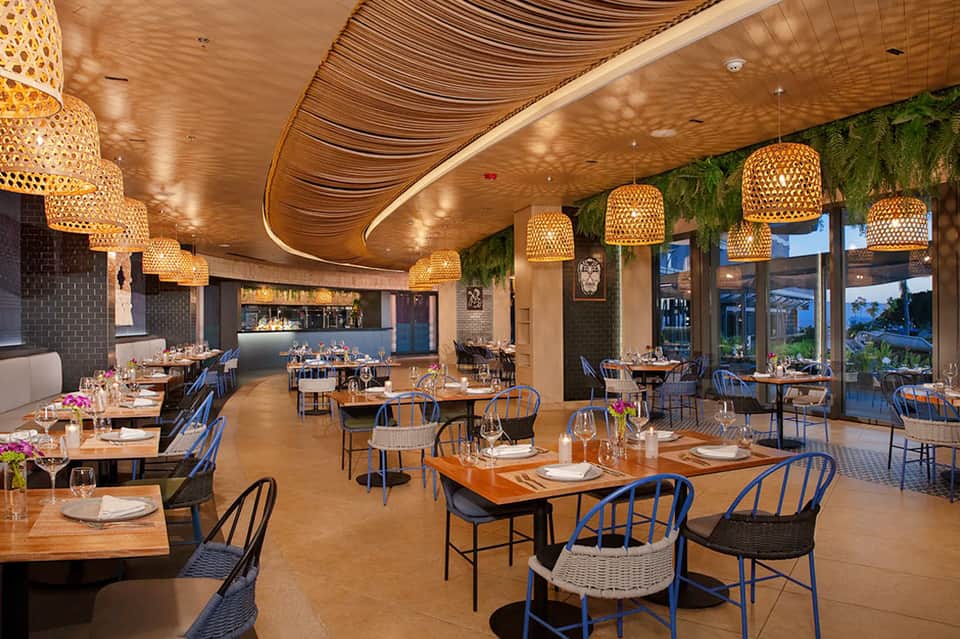 Modern upscale restaurant with woven pendant lights, wooden tables, and expansive ocean views