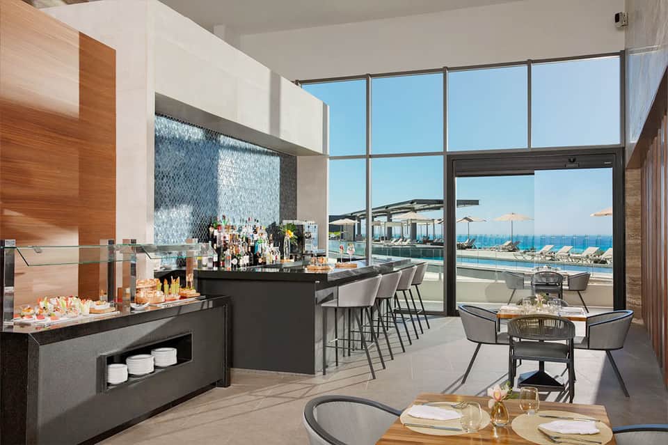 Modern rooftop bar and lounge with ocean views, black counters, and floor-to-ceiling windows