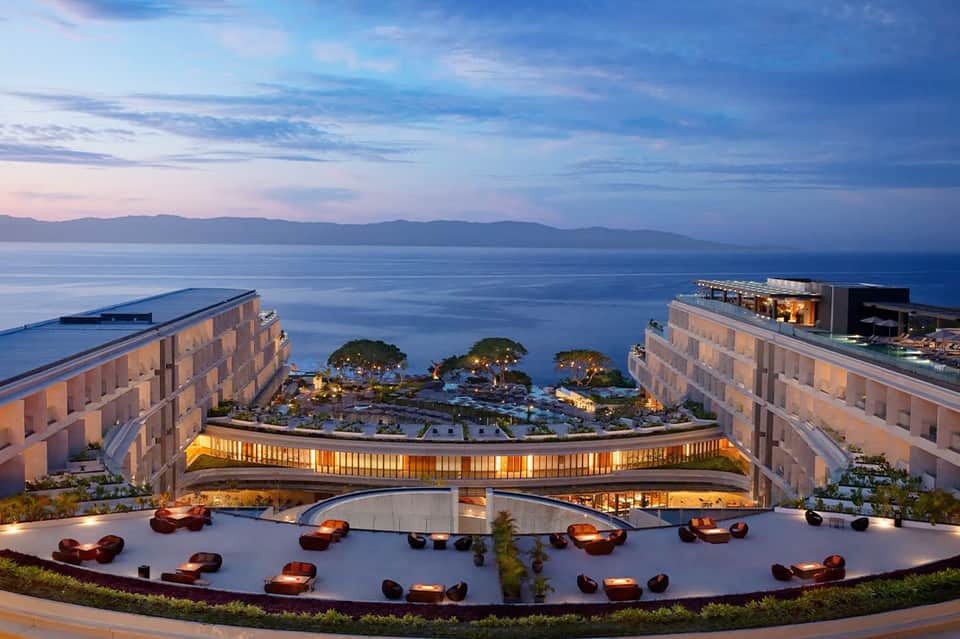 Illuminated resort terrace overlooking bay at dusk with fire pits and architectural design