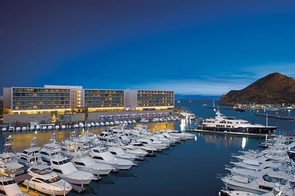 Marina at dusk with modern waterfront resort buildings and multiple white yachts moored alongside