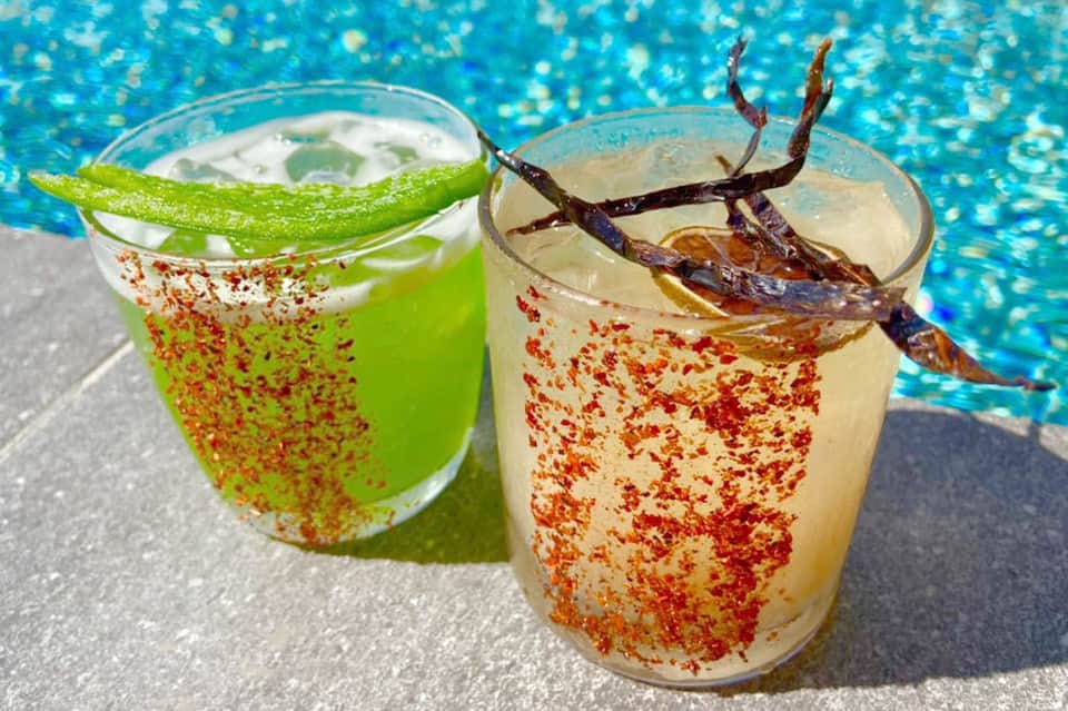 Two colorful tropical cocktails with spiced rim and vanilla bean garnish by pool