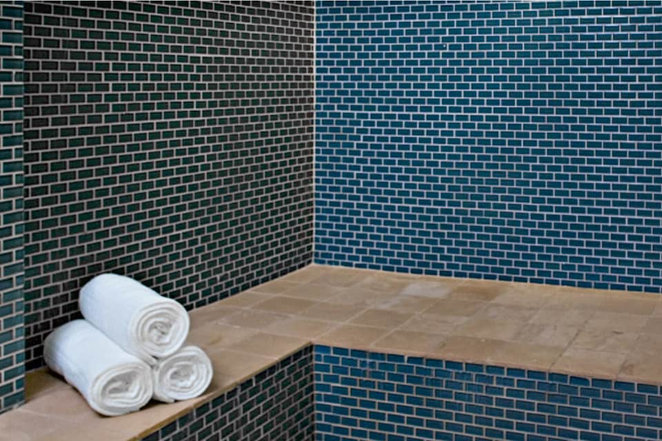 Spa shower area with teal brick walls, stone bench, and rolled white towels