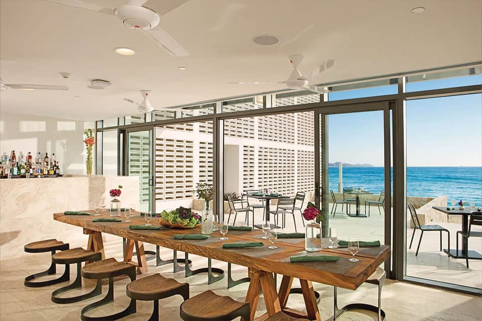 Modern restaurant interior with wooden dining tables, ocean views, and minimalist décor