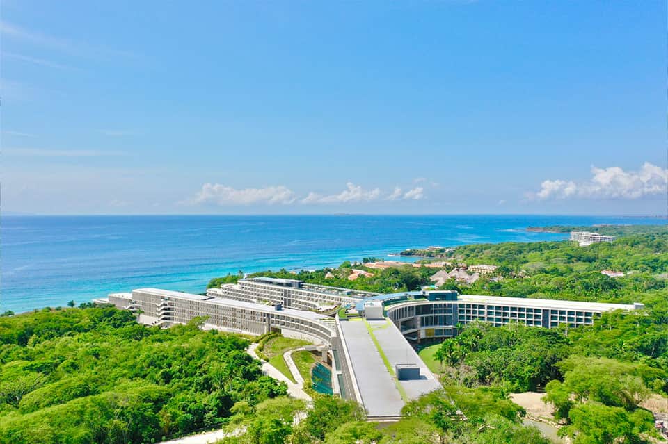 Aerial view of modern resort built into cliffside overlooking turquoise ocean and tropical landscape
