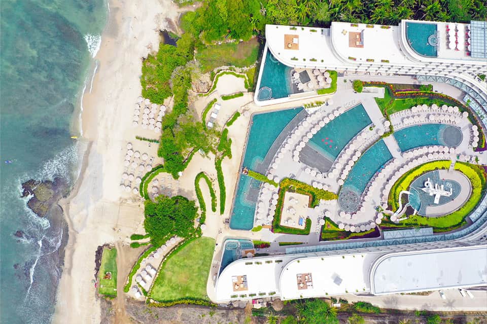 Aerial view of resort pools and white loungers on sandy beach with turquoise ocean