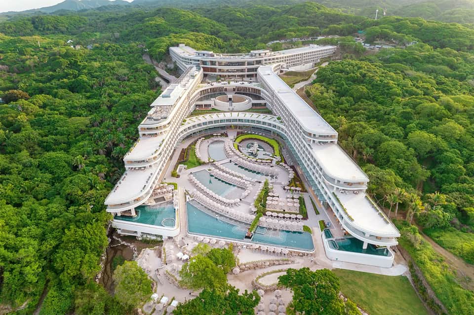 Aerial view of massive resort complex nestled in lush green mountains with multiple pools