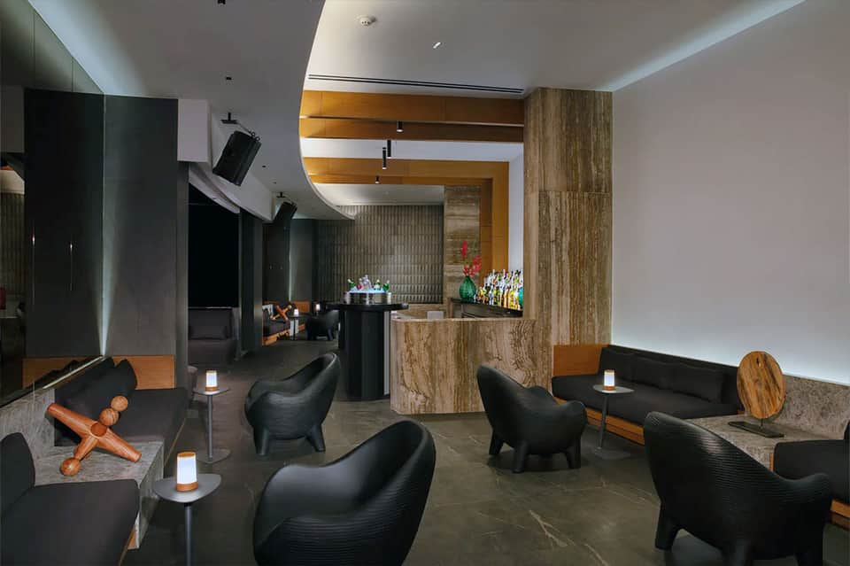 Modern resort bar and lounge with black sculptural chairs, wood accents, bar counter and ambient lighting
