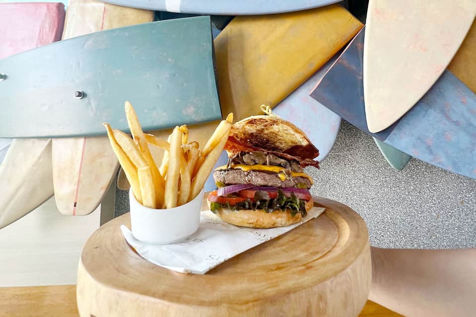Gourmet burger and fries served at poolside resort restaurant with colorful surfboards