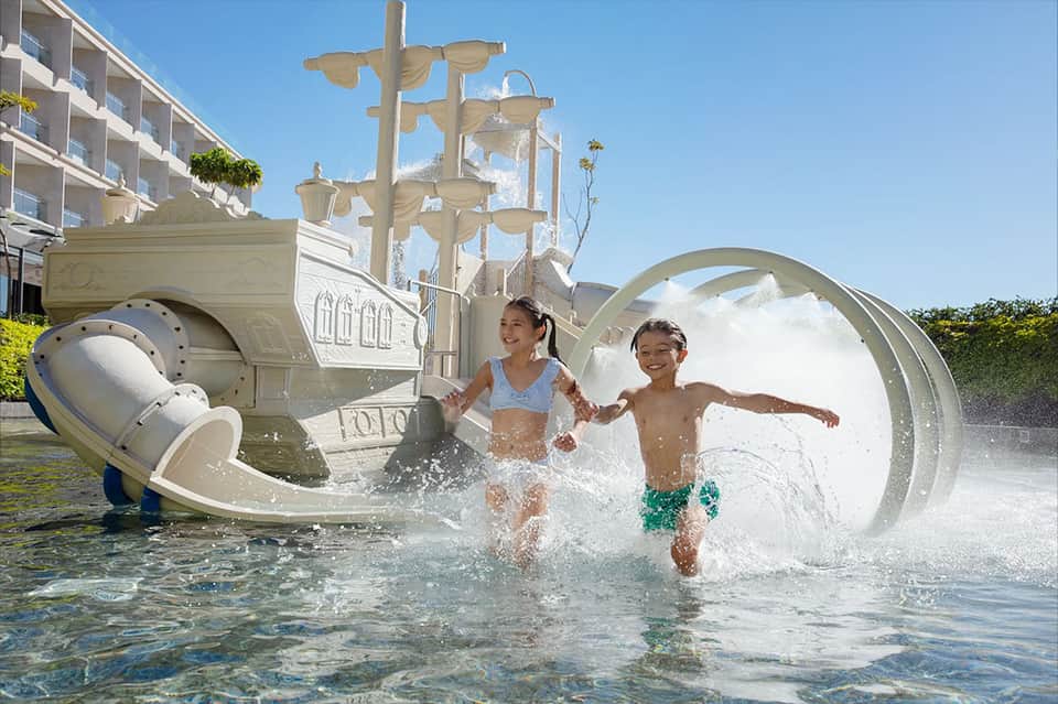 Children playing on elaborate ship-themed splash pad with water features and waterslides