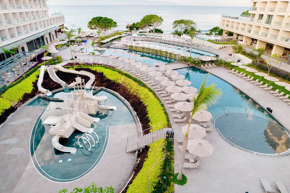 Aerial view of multi-tiered resort pools with loungers, beach access, and ocean horizon