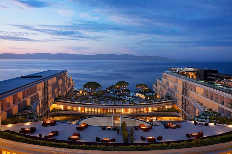 Luxury resort terrace at dusk with fire bowls, curved architectural elements, ocean and mountain views