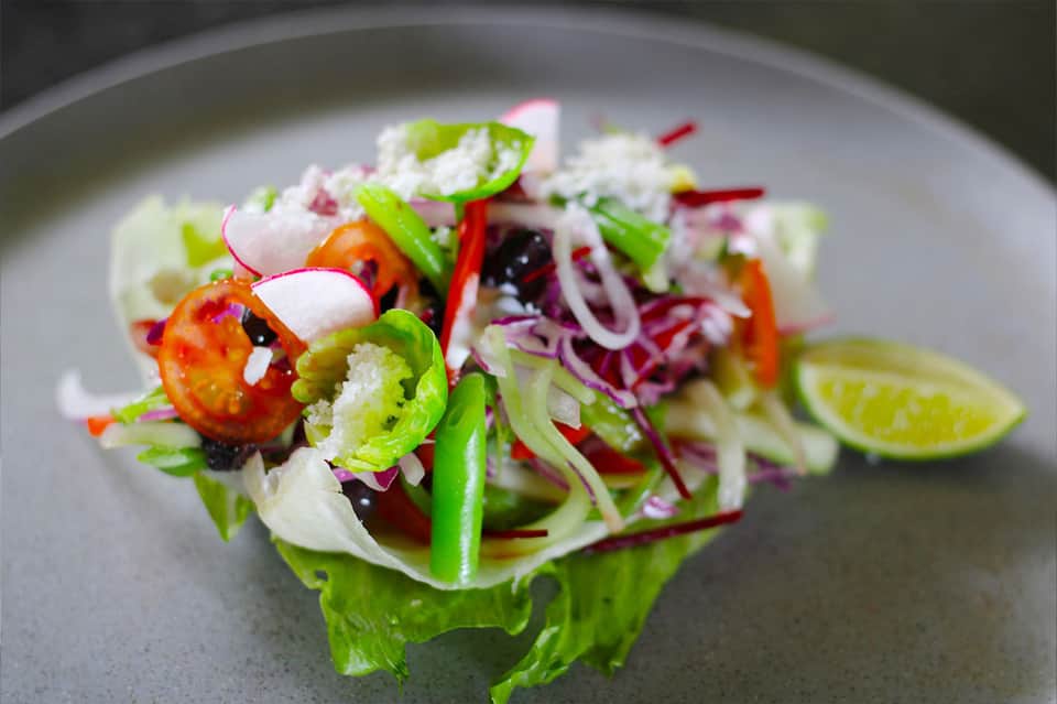 Gourmet plated salad with fresh vegetables, microgreens, and lime garnish on a gray plate
