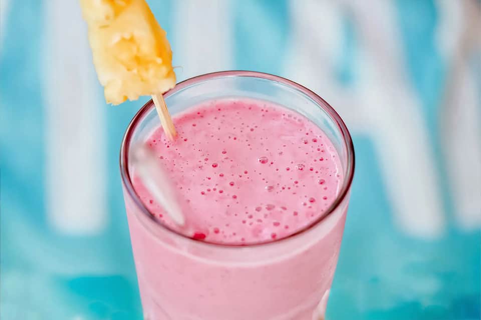 Pink smoothie or açai bowl with pineapple garnish against turquoise background