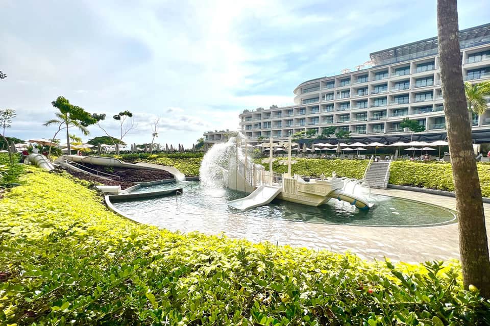 Resort water feature with cascading fountain and slide, lush green landscaping, modern hotel