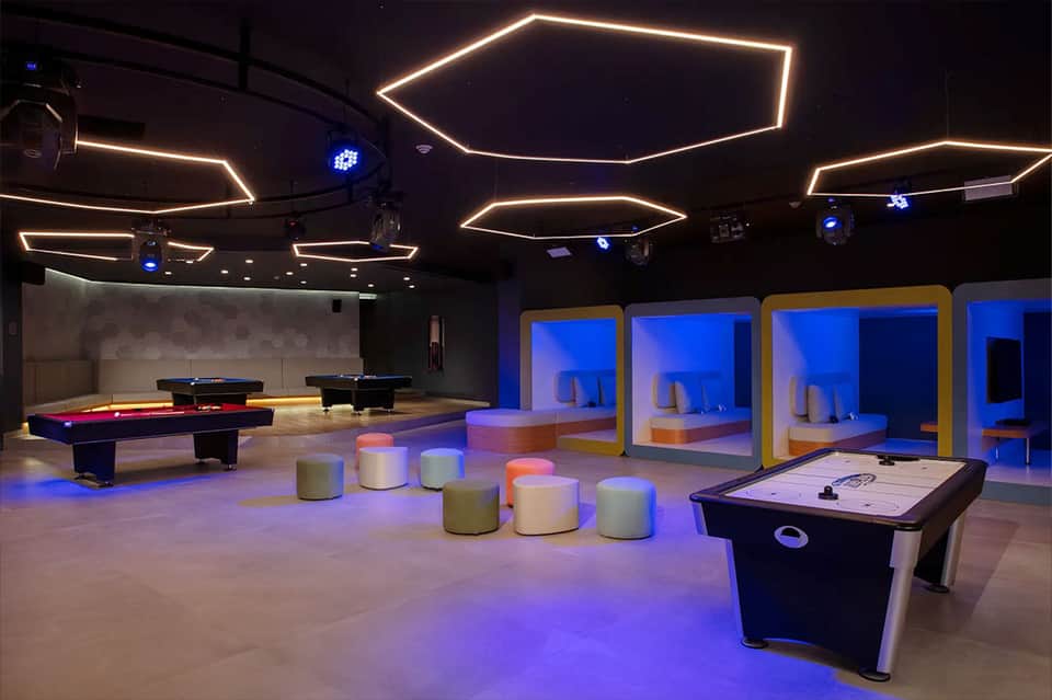 Modern entertainment lounge with neon-outlined geometric ceiling fixtures, pool tables, and illuminated seating areas