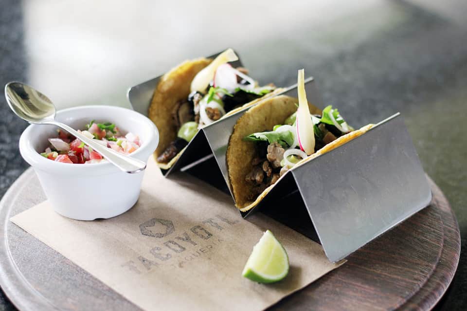 Three tacos with pico de gallo and lime on a wooden serving board