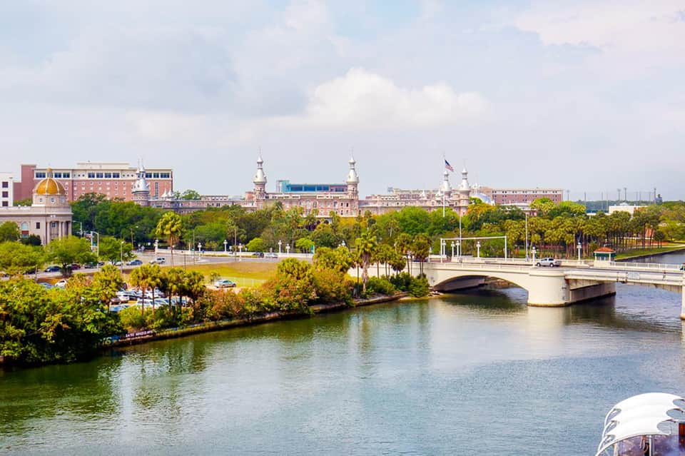 Aerial view of riverside cityscape with historic buildings, bridges, palm-lined waterfront and green spaces