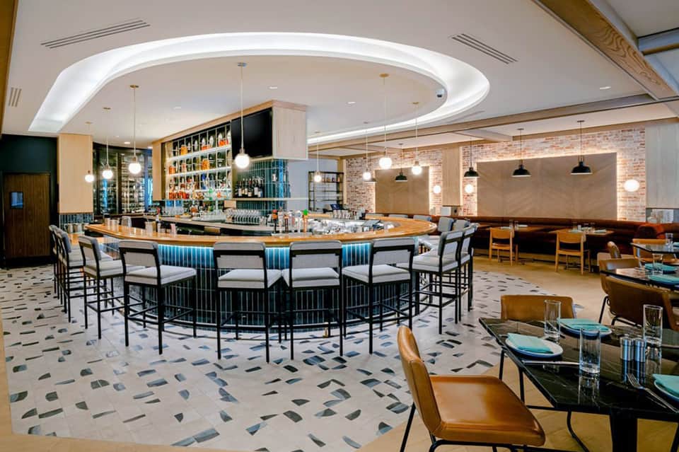 Contemporary bar lounge with curved counter, pendant lights, brick accent wall, and patterned flooring