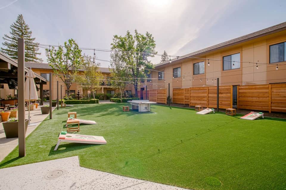 Hotel courtyard with artificial turf lawn, cornhole games, and modern residential-style buildings